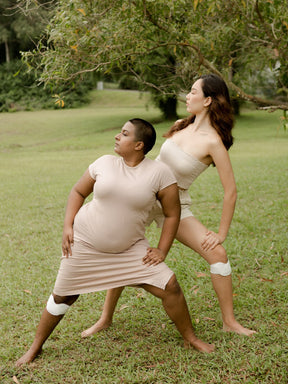 two women using kneeheat while stretching on an empty field